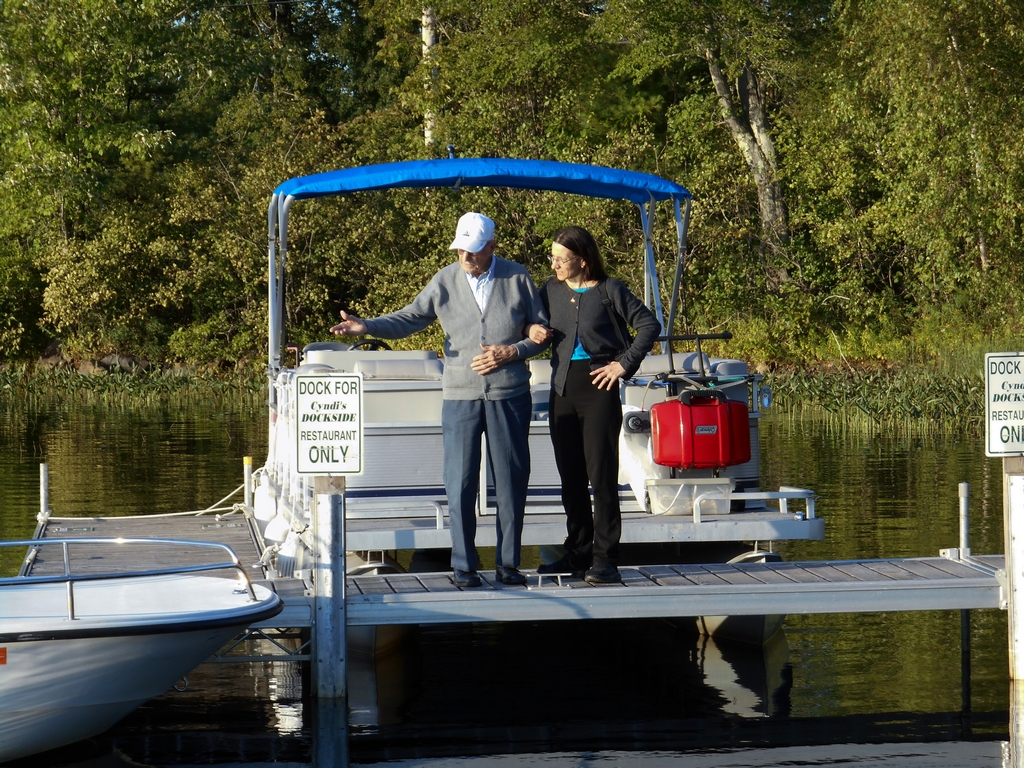 Gerry and Anne standing together on the dock at Cyndi's Dockside with a pontoon boat behind them