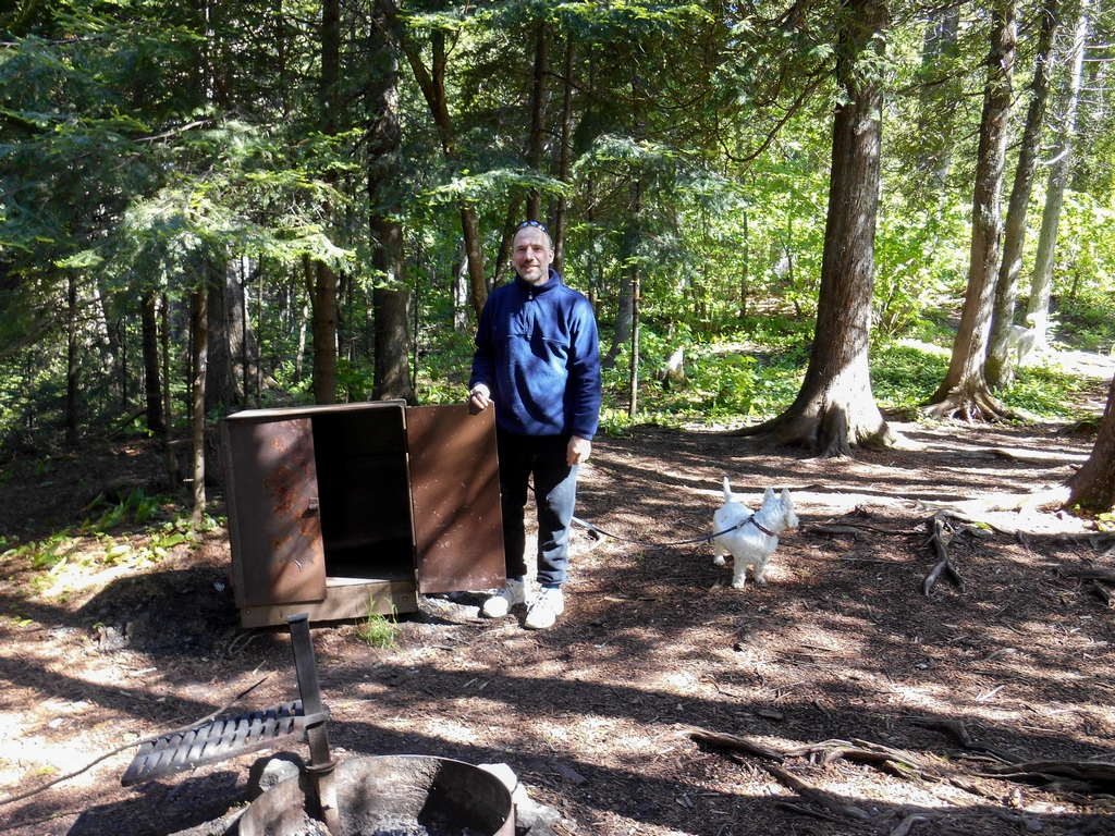 Paul standing beside a metal bear box at a campsite in George H. Crosby Manitou State Park while Fritzy waits on leash nearby