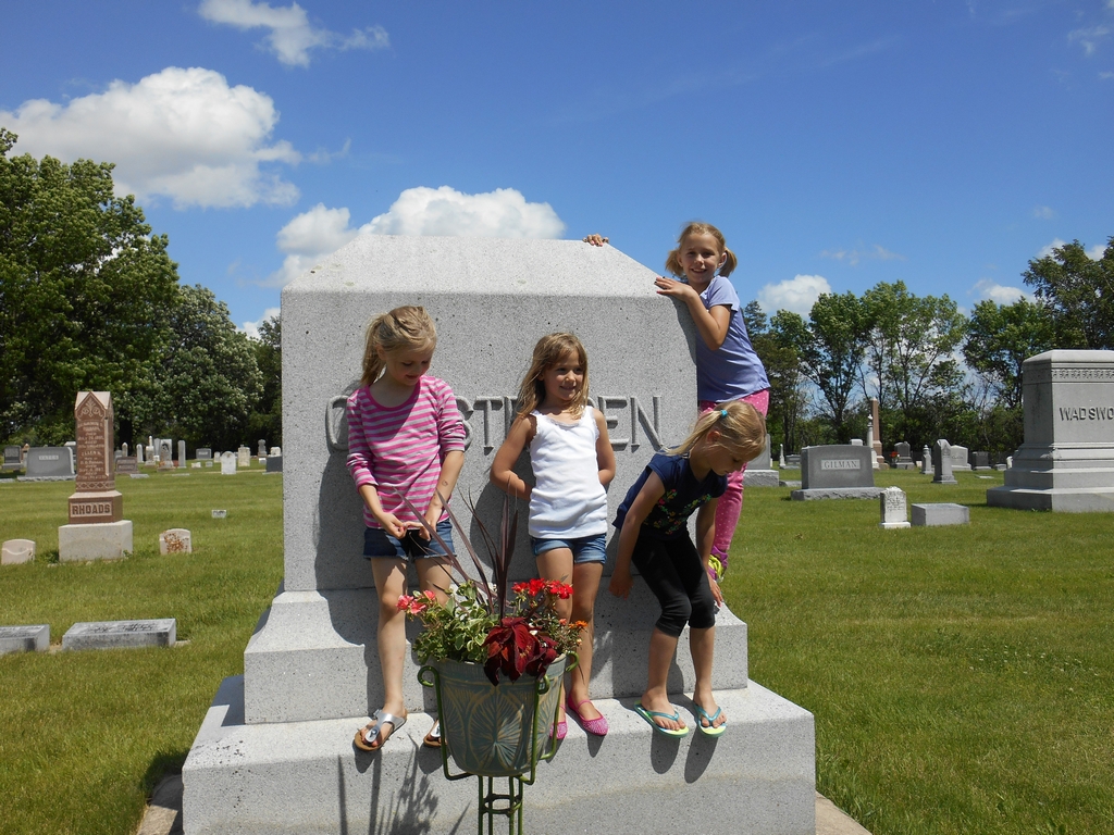 Four girls climbing and posing on the Christensen grave marker in the cemetery