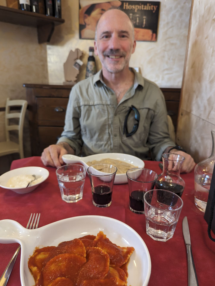 Paul on the other side of a lunch table, with 2 plates of ravioli and some glasses of wine on the table