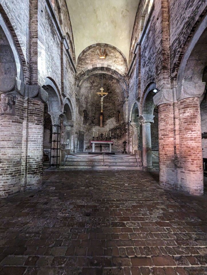 An old, stone and brick church, looking down the center at the altar with a cross above the altar.