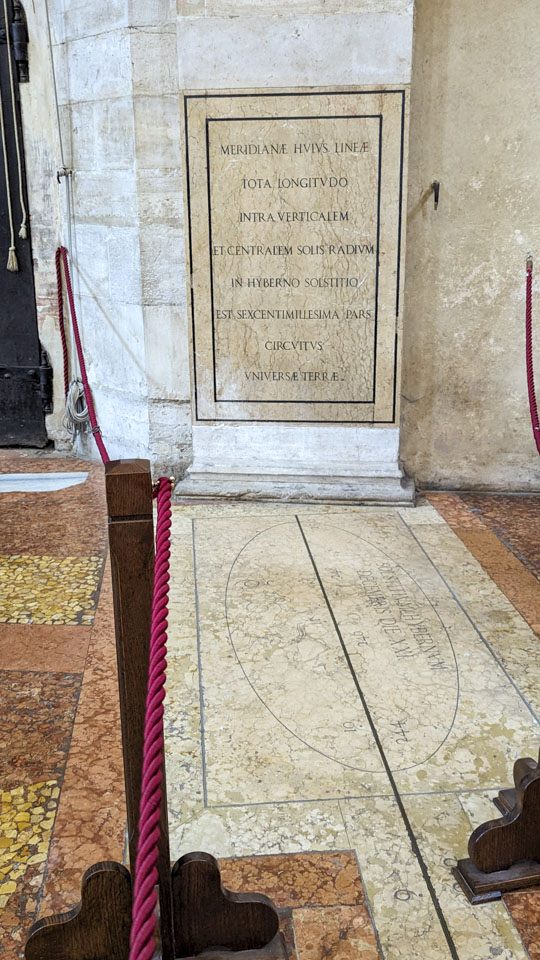 A marble plaque in Latin about the meridian line, and the start of the line itself.