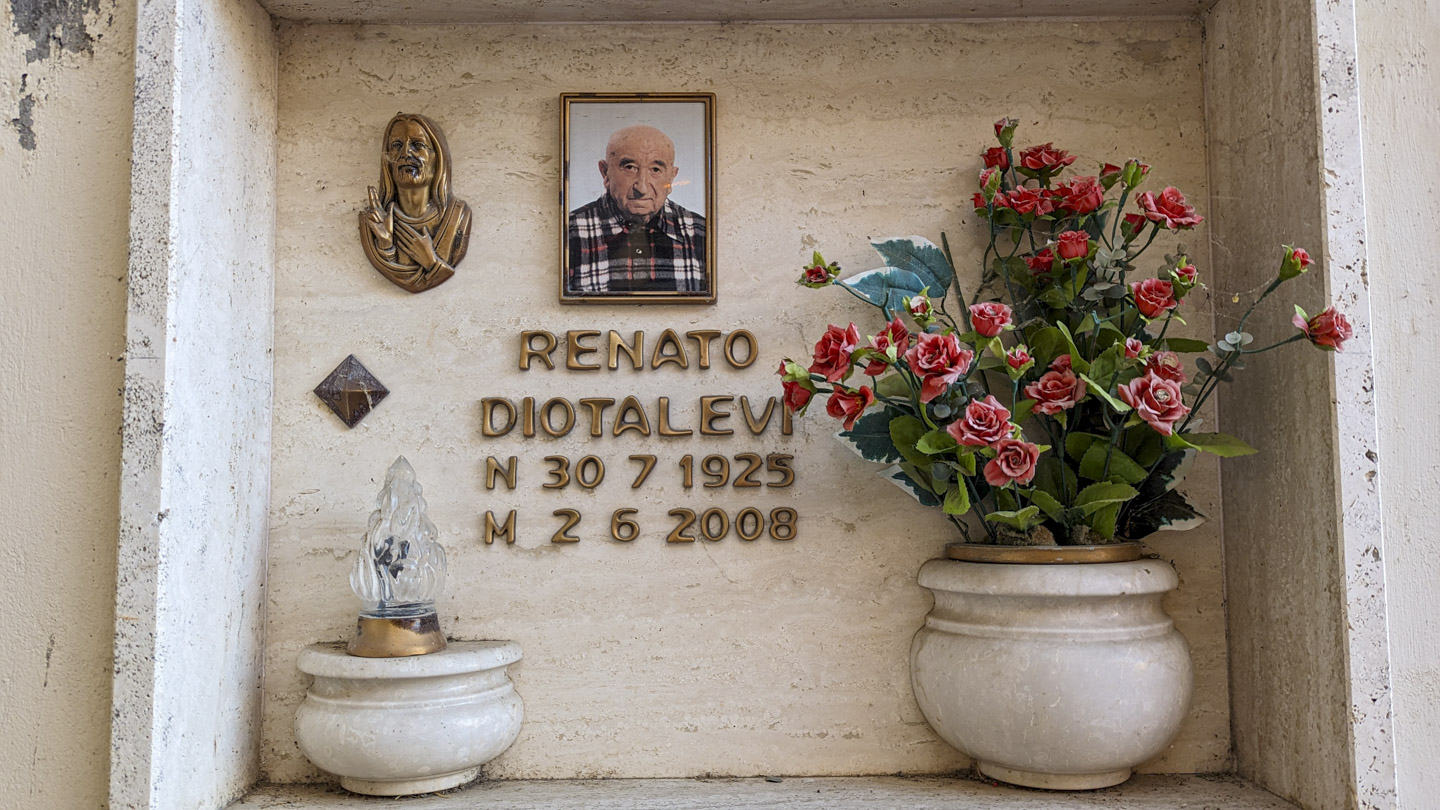 Faceplate of Renato Diotalevi's tomb. Artificial flowers are in a built-in vase on the right. There is a color picture of him wearing a plaid shirt.