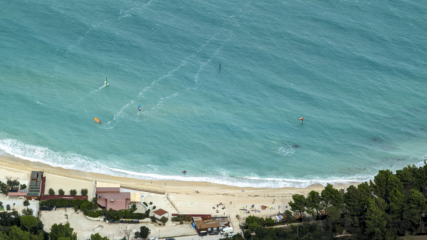 A gently curved beach with richly colored green water with surfers in the water.