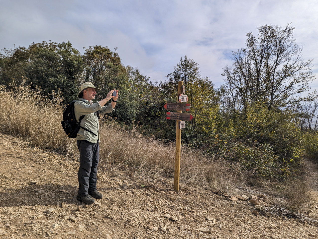 Paul is standing next to a sign while taking a picture on his smartphone.