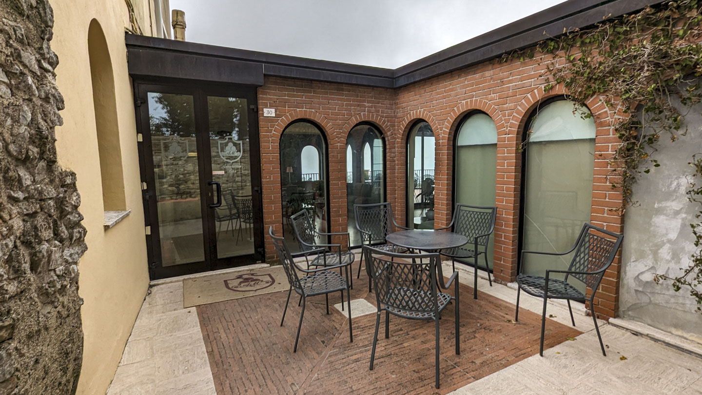 An alcove off the main courtyard with a round metal table and 6 metal chairs around it. The walls are modern brick with large windows and a glass door.