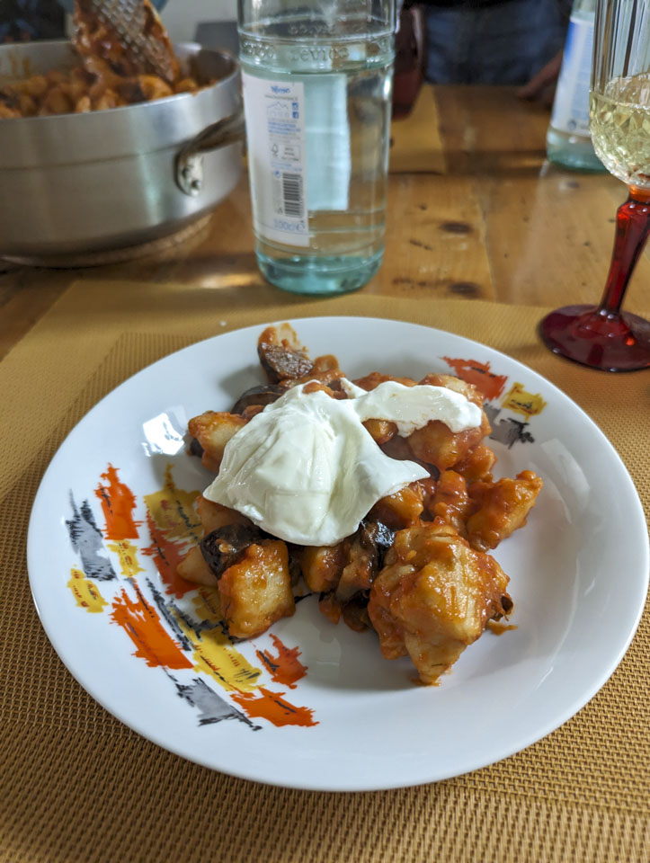 A white place with a random painted design has large gnocchi on it with eggplant and burrata.