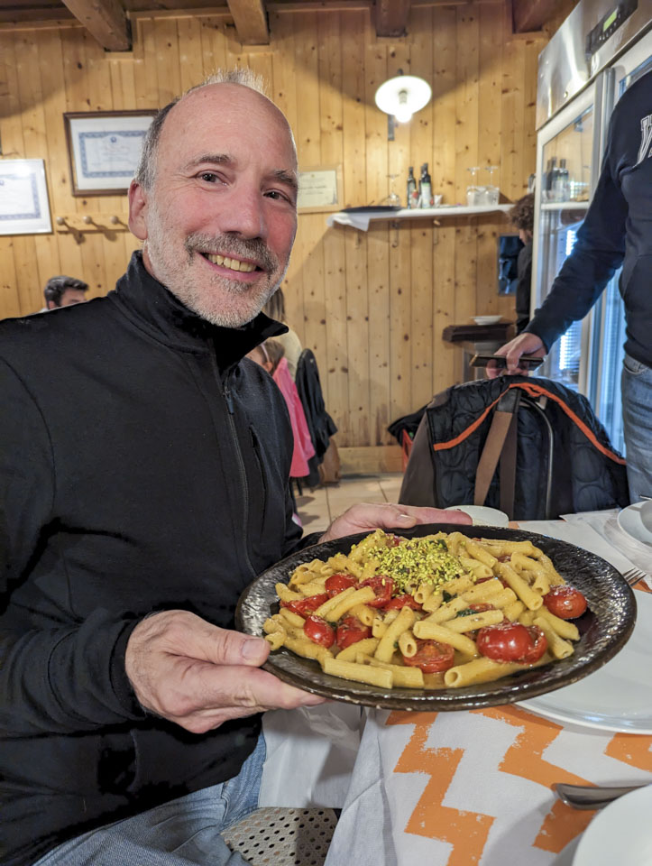 Paul is holding a plate of pasta with tomato and chopped pistachio