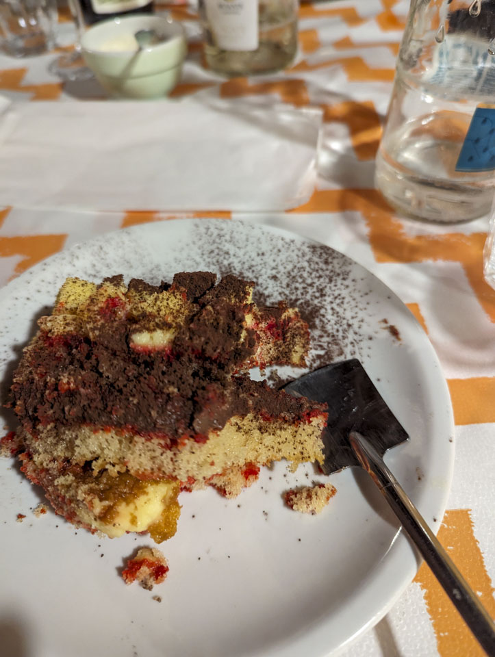 A white plate with a cake on it and a little spoon that looks like a flat shovel.