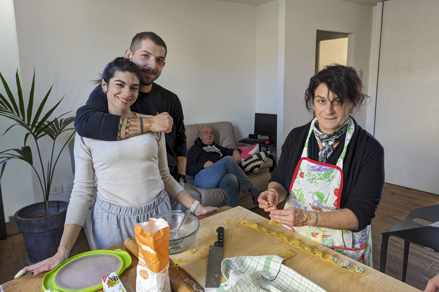Flo and Dodo are standing near the table, Francesco is sitting on the sofa in the background, and Doni is working on assembling ravioli.