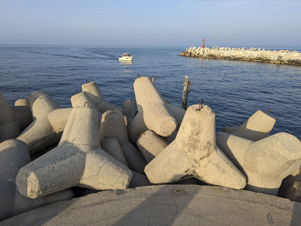 Looking out over some 4-spiked breakwater barriers at a boat coming into a canal