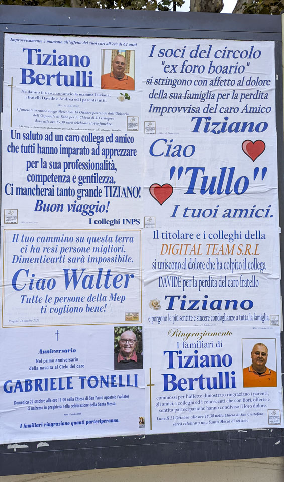 A large board with memorials posted to deceased people. There are 8 spots, and 4 of the spots have signs dedicated to Tiziano.