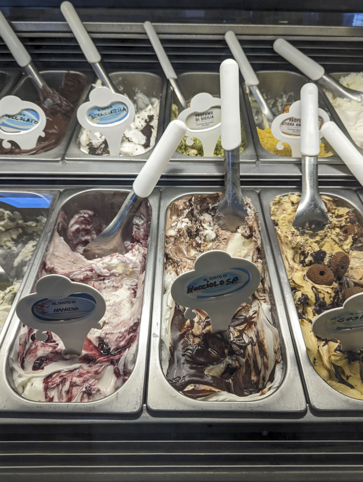 Oblong metal containers with various fancy looking flavors of ice cream.