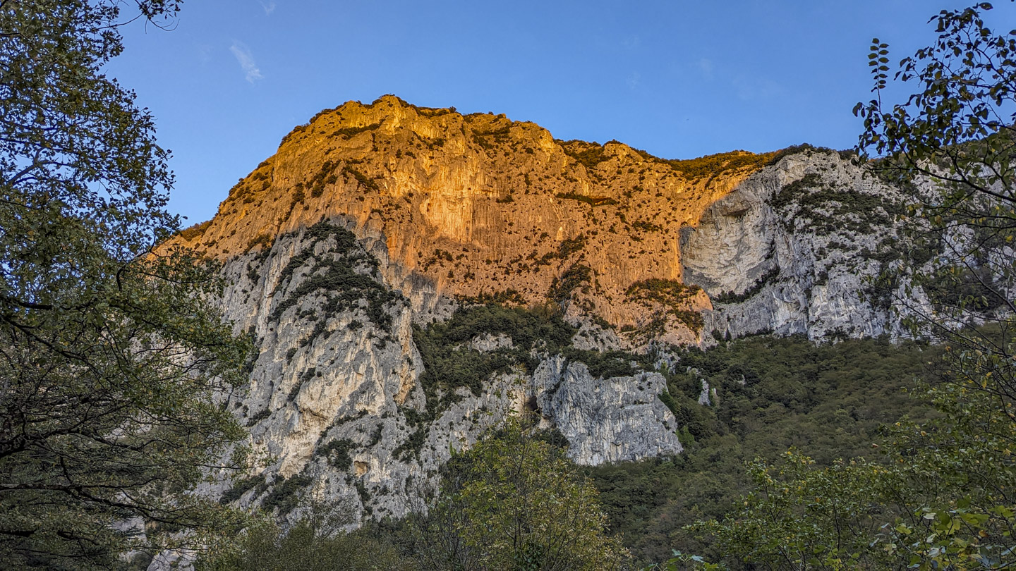 A blue sky with the top of a cliff bathed in golden light, while lower portions have a gray color.