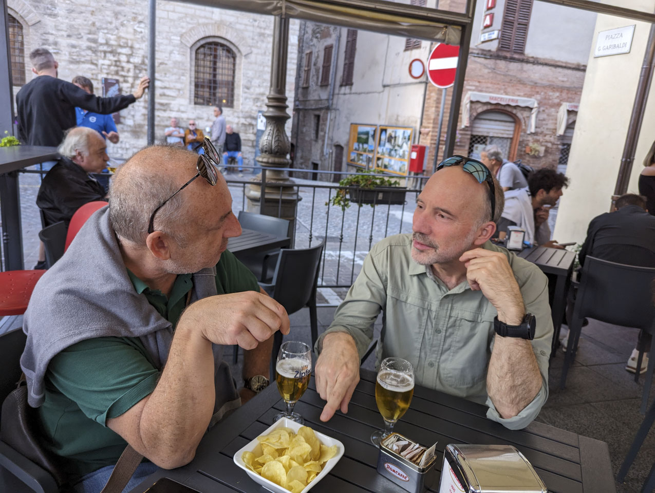 Francesco and Paul seated at a table and having a conversation, with some potato chips and each with a glass of beer
