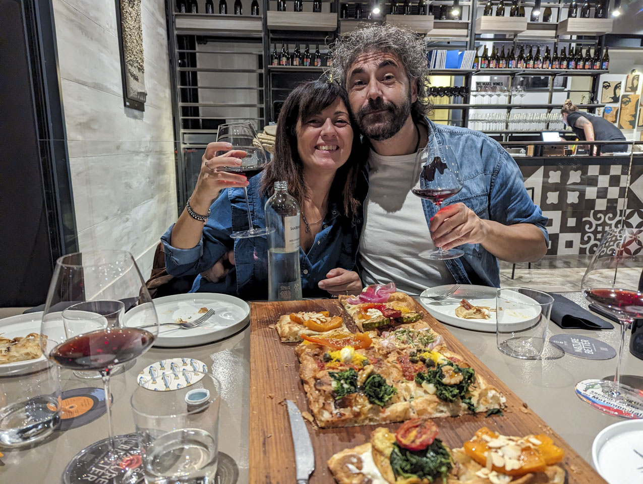 Valentina and Federico with a large focaccia in front of them, holding glasses of the vineyard's wine