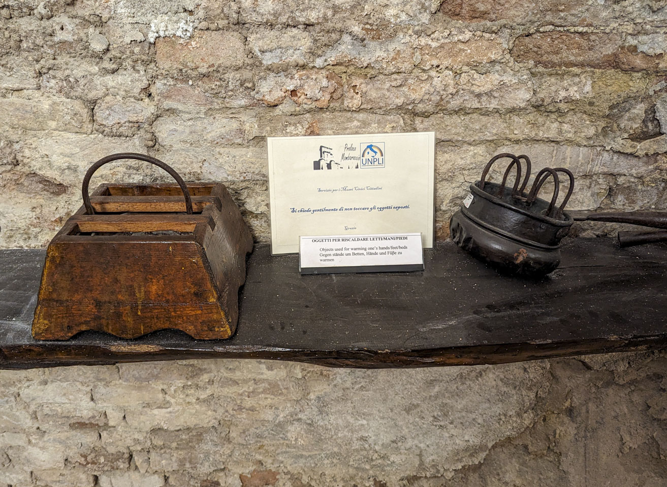 A shelf with two objects. One is wood and roughly square with a handle in the middle and space for hot coals. The other is a metal bowl with handles.