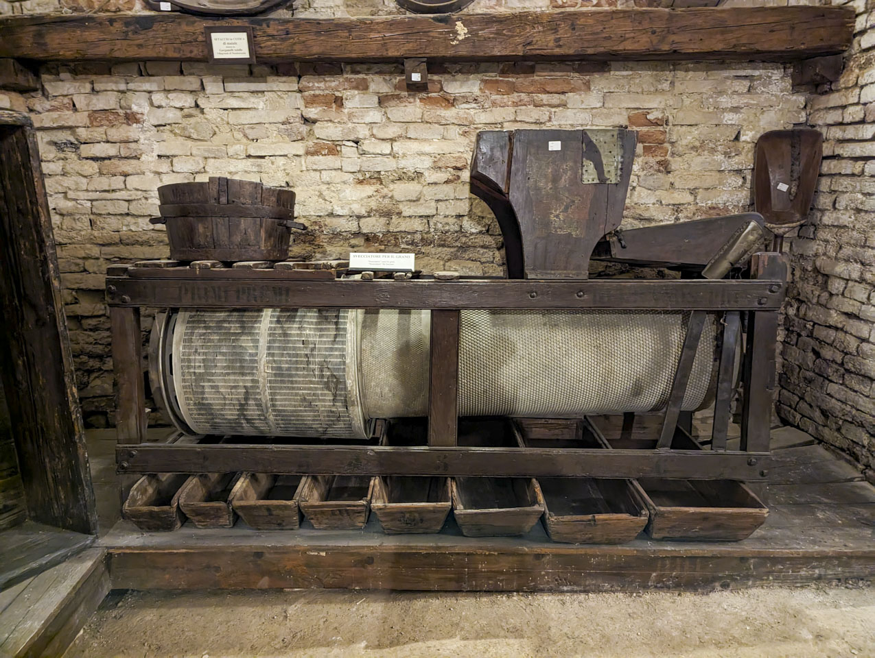 A wooden frame that has large perforated rollers in it, with perforations of different sizes, and wooden bins underneath to collect what falls out.