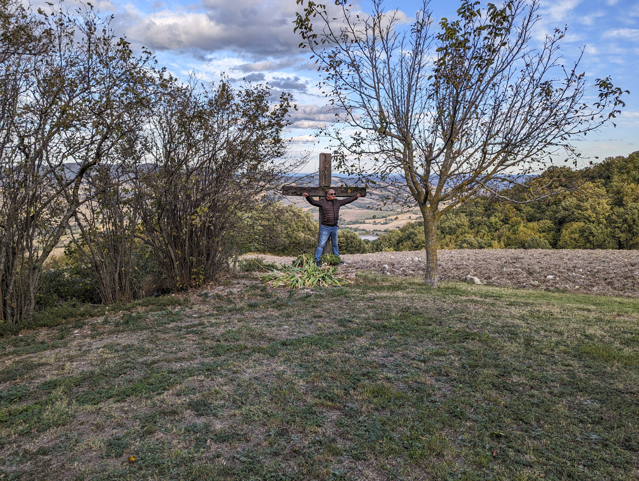 Francesco standing in front of a wooden cross, with his arms spread wide.