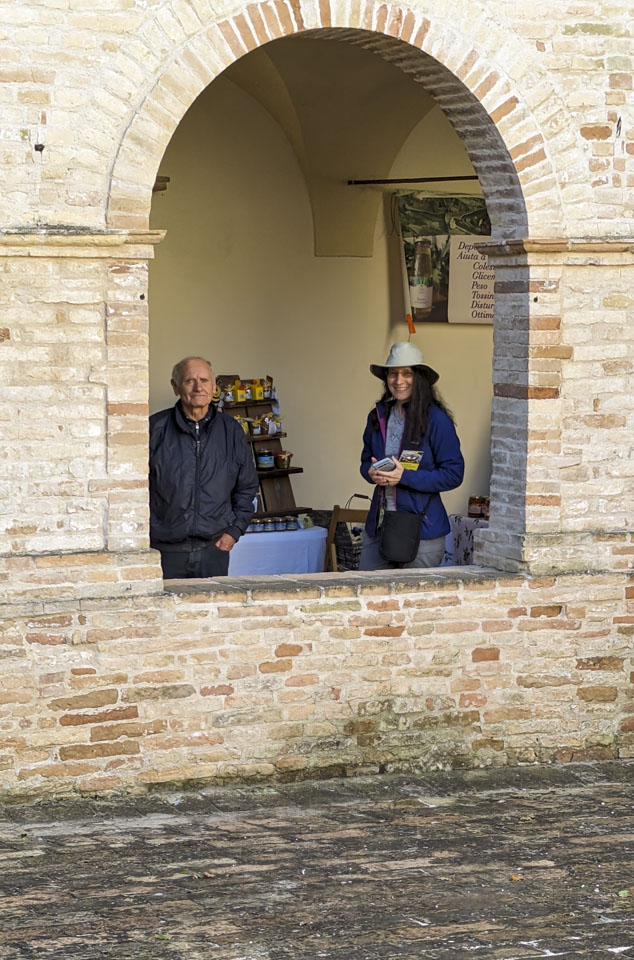 A man and a woman seen through an open arched window that is in a stone wall.