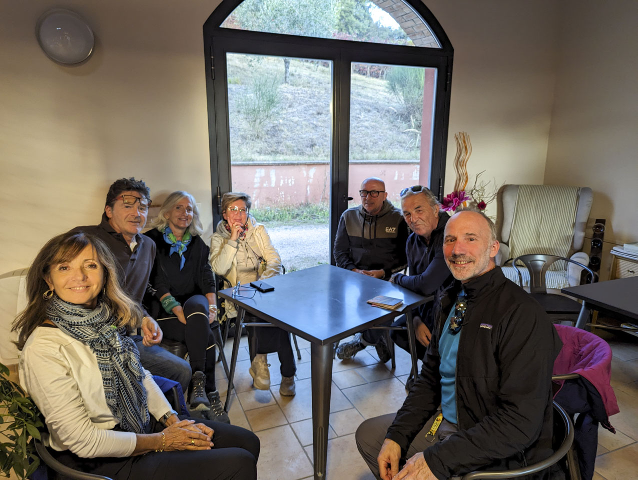 People sitting at a table; behind them are large glass doors leading out of doors.