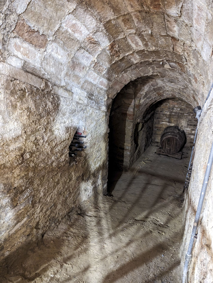 View of the grotto beneath the Offida museum with stairs going down, wine bottles tucked into a hole in the wall, and a large barrel in an alcove at the bottom.