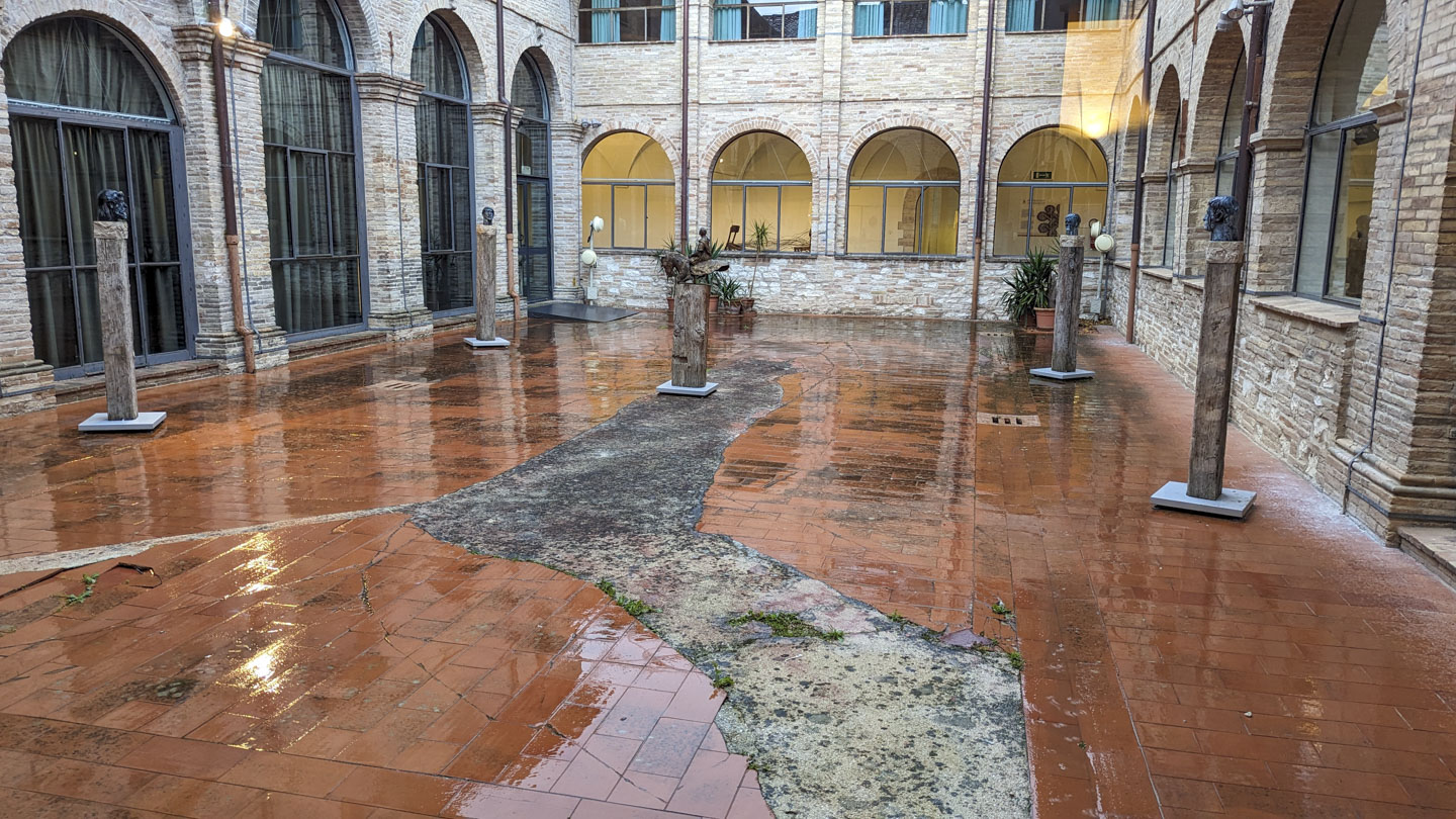 A red brick atrium with nice stone walls. In the atrium are many pedestals with busts of people and a small model of one of the bronze figures.