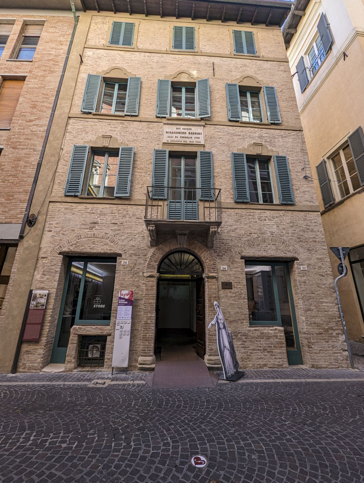 A 4-story stone building with 3 windows on each of the upper levels and a small balcony on the second floor. There is a cut-out figure of an opera performer outside of the entrance.