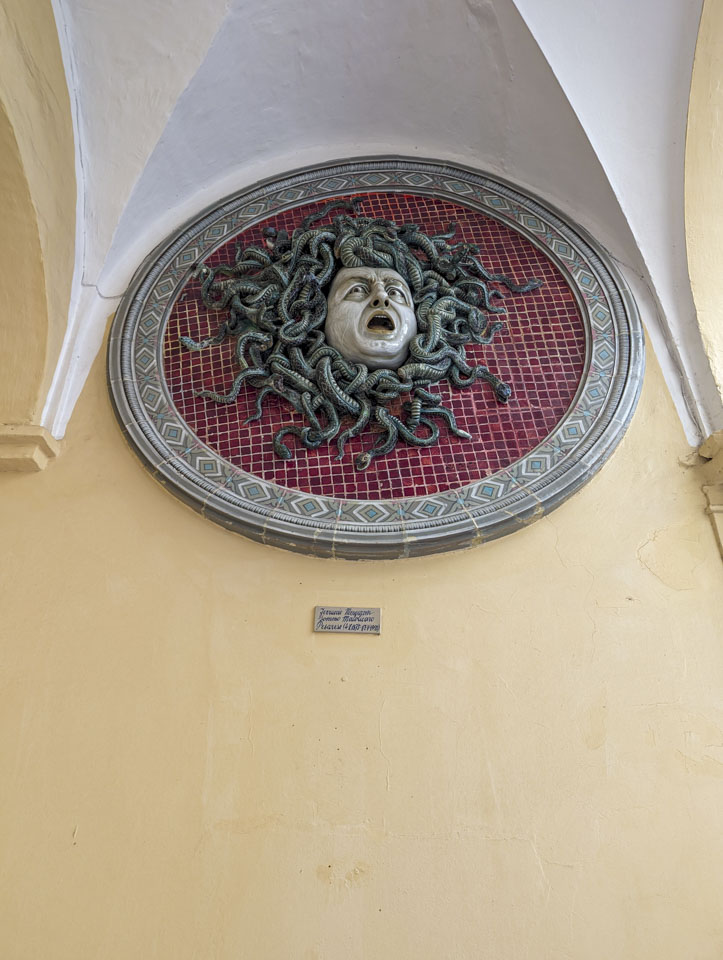 Looking up at a large round plaque with a sculpture of a frightened looking face surrounded by snakes. 