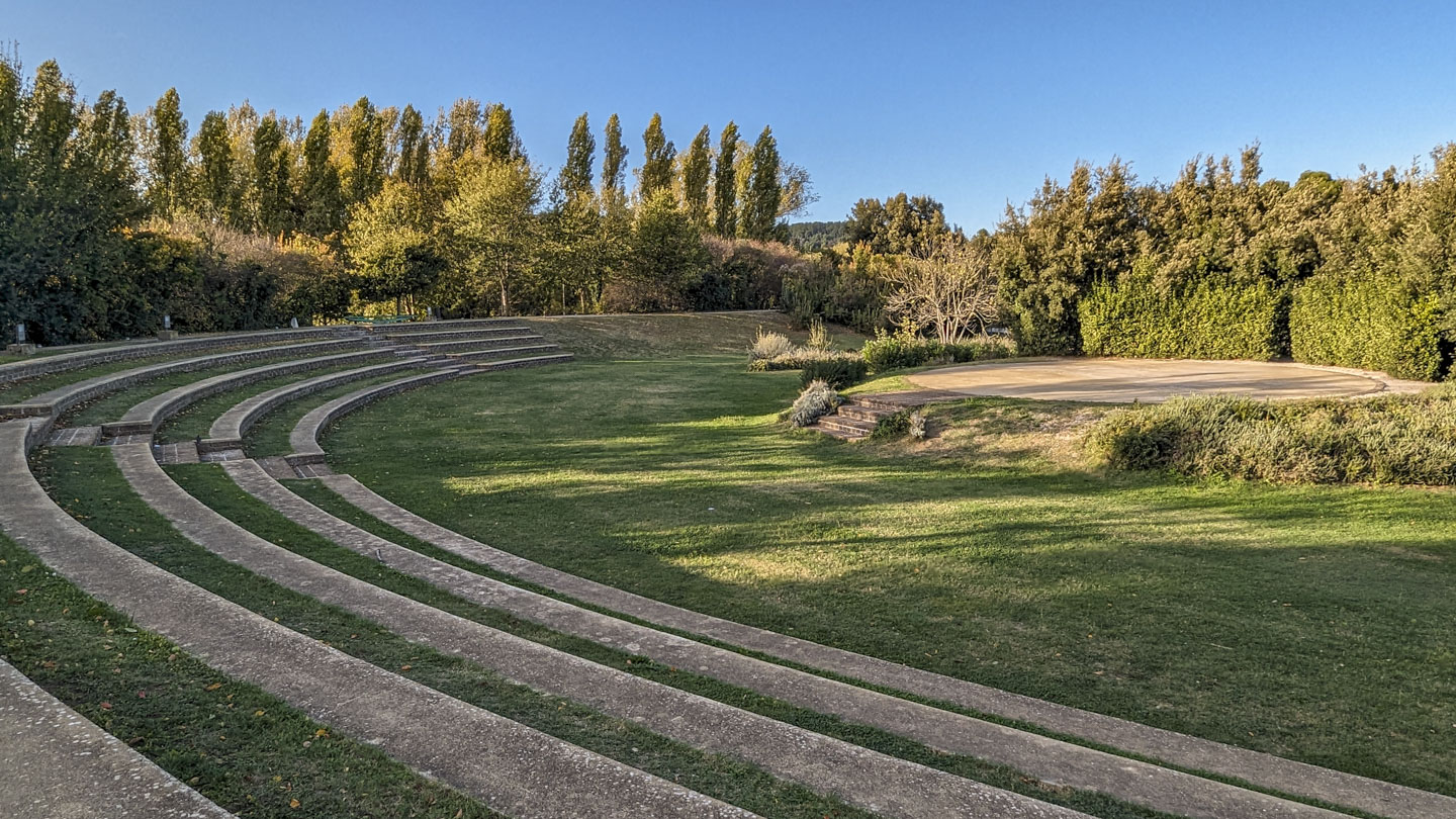 A round stage is on the left, with a grassy area between it and some long curved cement tiers.