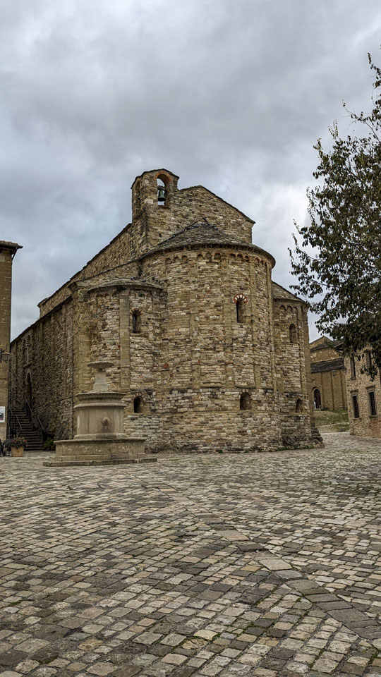A stone plaza with a stone fountain and a stone church. The sky is gray and cloudy.