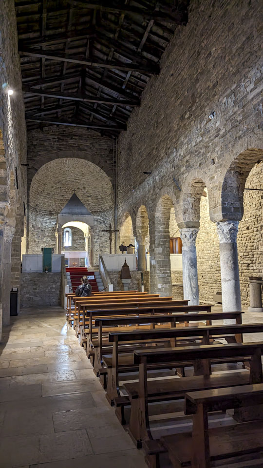 Anne can be seen in a wooden pew, with stone columns on each side, and an altar that is on a platform at the end of the church.