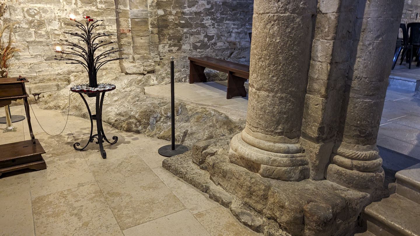 A tree-shaped candle holder is on the left, and the base of a column is on the right. Around the base of the column and between slightly offset levels the bedrock can be seen..