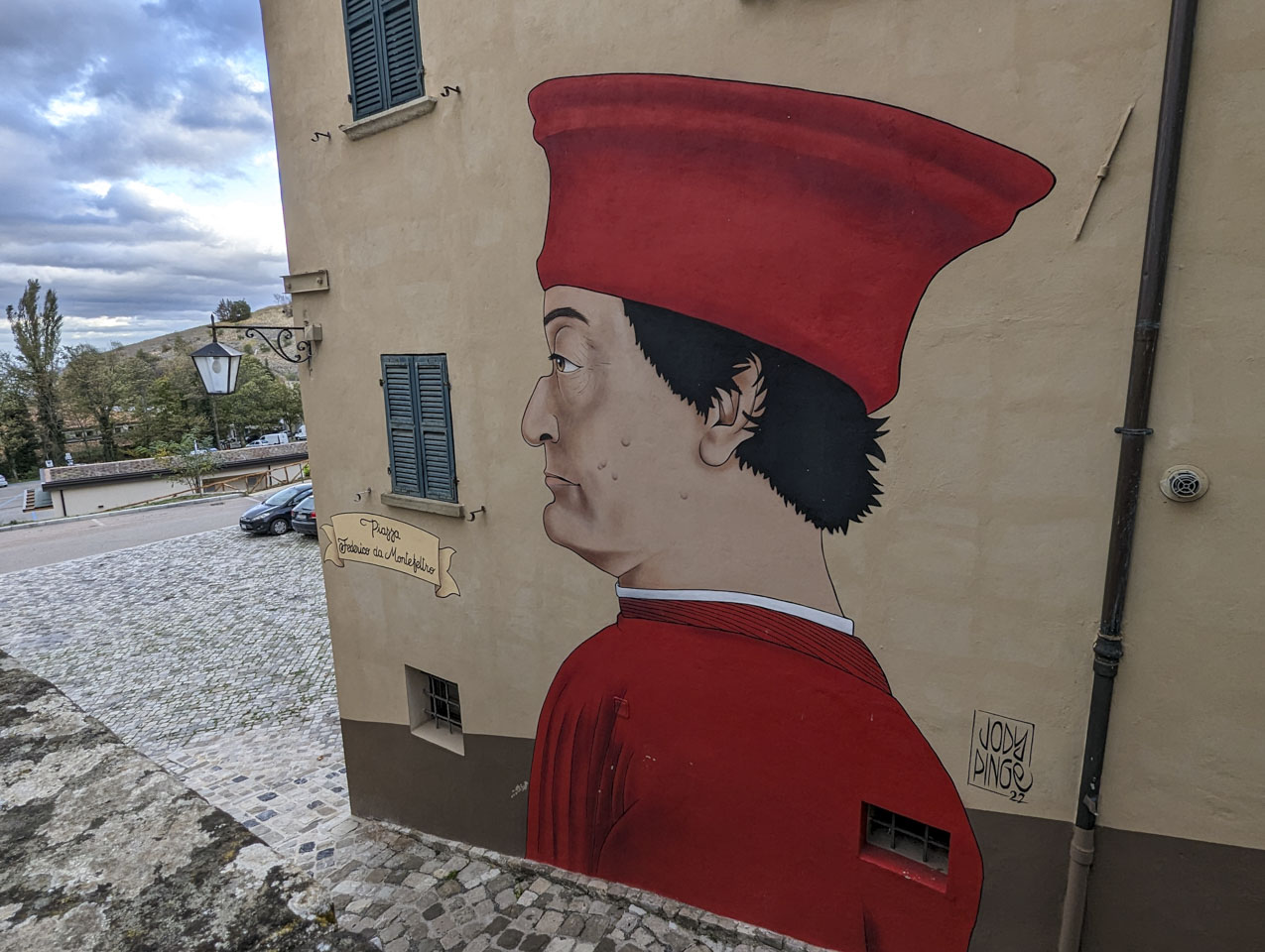 On a tan wall is a drawing of a man in profile. He wears a red hat and jacket, ahs short dark hair, and an oddly steep nose.