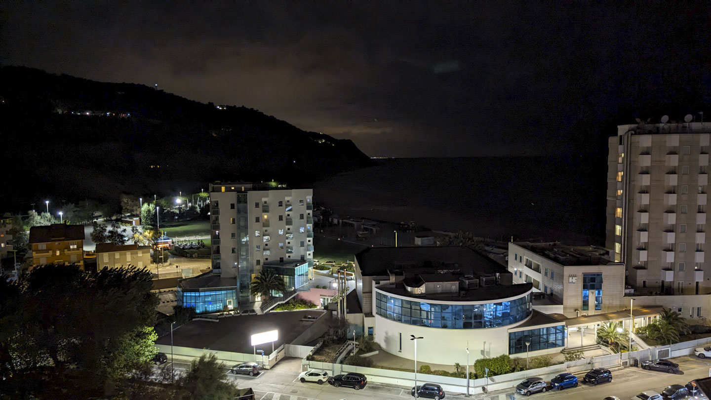 Looking out from an upper story, the large dark outline of a high hill is on the left, and on the right is the flatness of the Adriatic Sea. In the forground are some modern looking buildings.