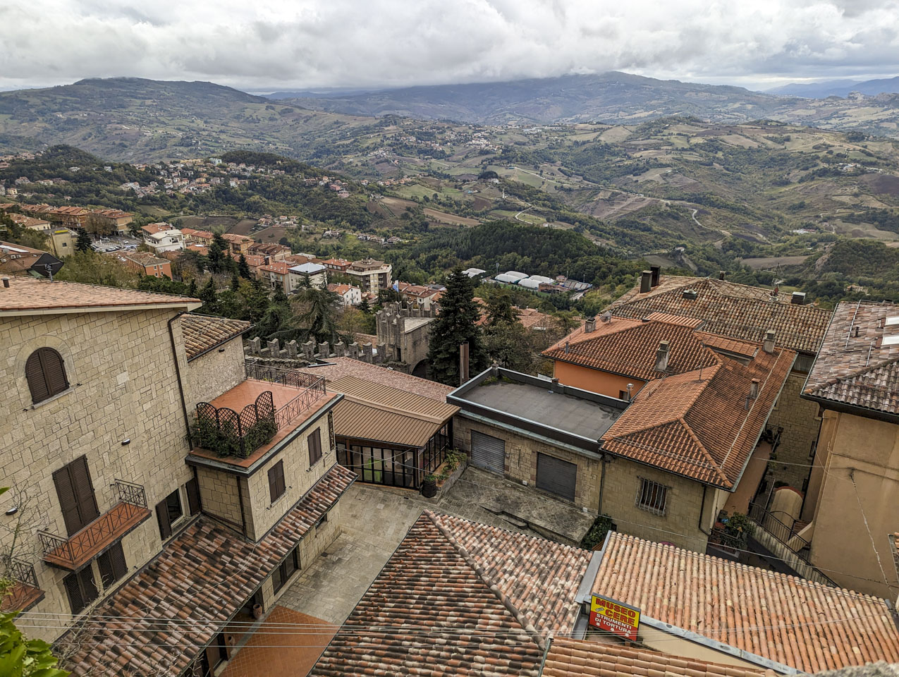 Looking at the tops of houses that rise up from the descending mountainside, with an undulating landscape as far as the eye can see.
