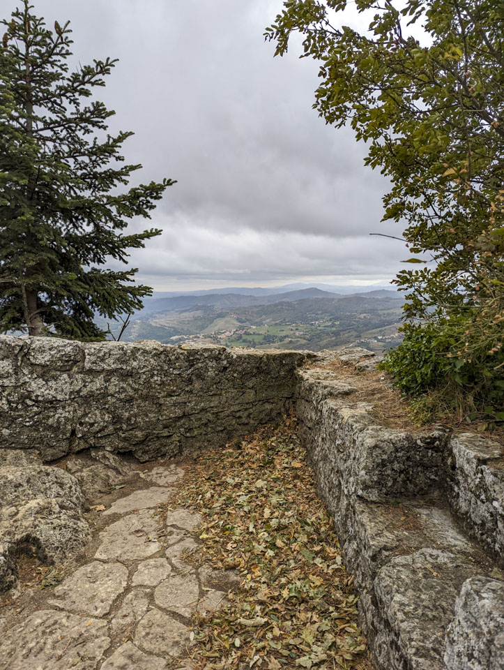 Two low stone walls that come to a point with the view of a mountainous landscape far below us.