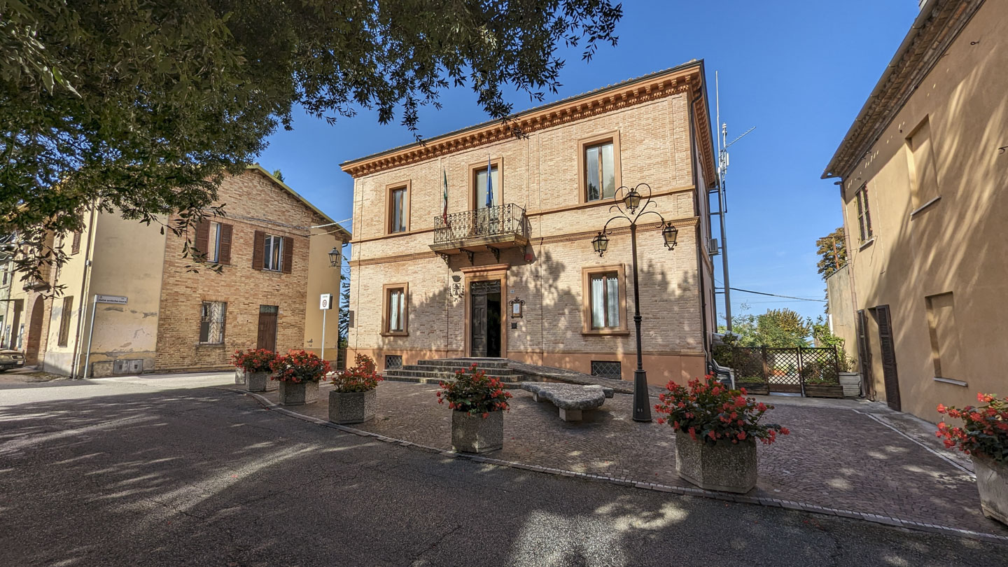 Stone building with large pots of flowers in front and an open door.