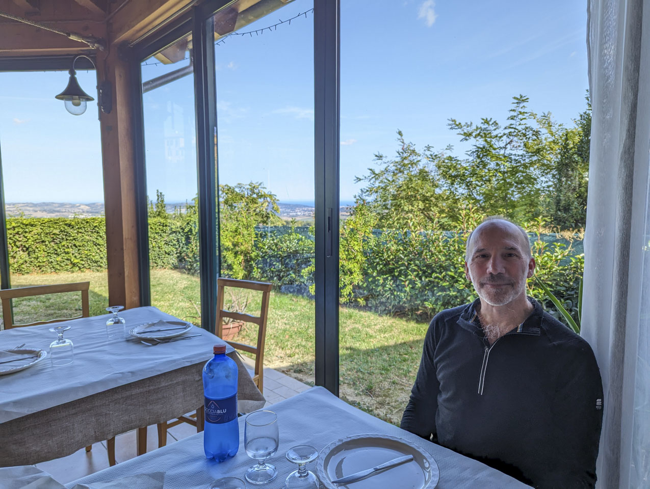 Paul sitting at a restaurant tale in front of windows. The sea can just be seen in the distance.