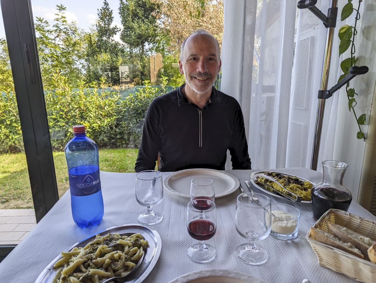 Paul in front of a restaurant table, with two glasses of wine, some bread, and two different pasta dishes.
