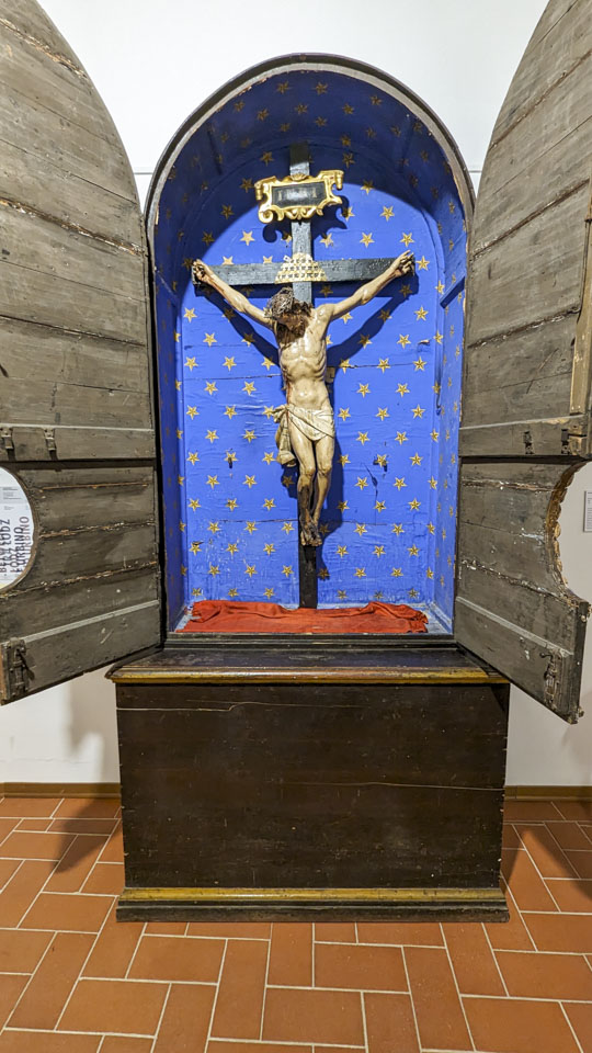 A statue of Jesus on the cross is in a box that is painted with gold stars on a blue background. The box has doors that have been swung open.