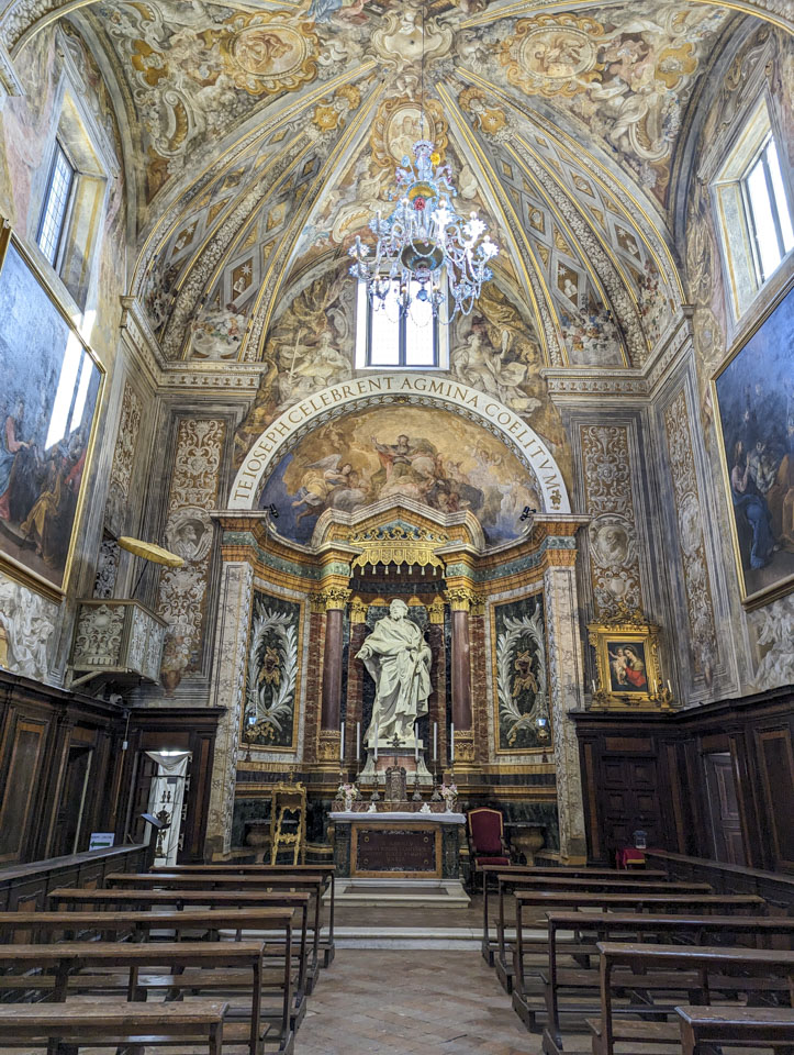 Standing between two rows or church pews, looking down at an altar and a large statue. The room is as described above, although you cannot see the organ.