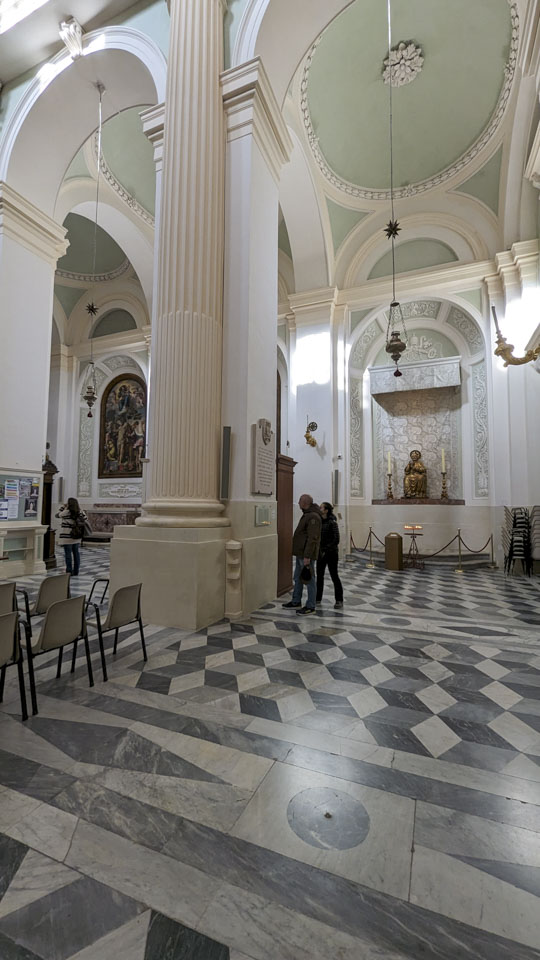A black and white block-illusion floor of the church catches the eye. The ceilings are high and rather plain, with pale green paint.