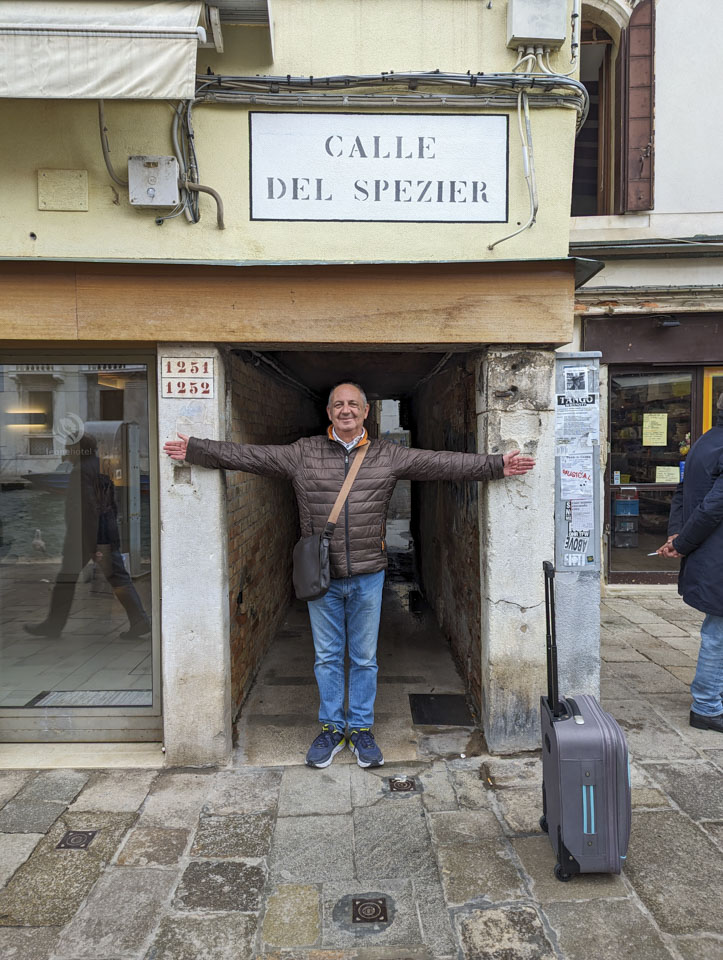 Francesco standing in front of the entrance to a street in Venice; the entrance is narrower than his armspan.