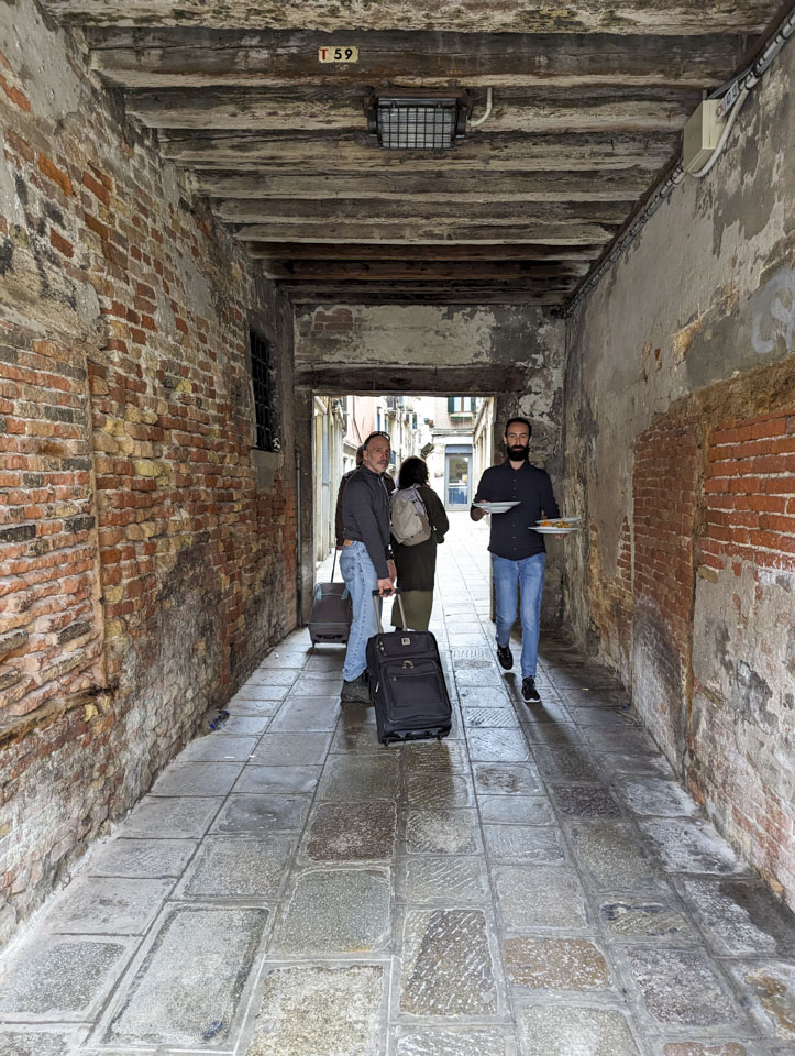 Paul with our suitcase, Francesco and Doni behind him, and a tall slim man coming towards us carrying three plates of food.