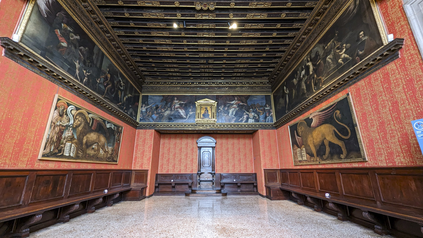 A room with red walls and a painting on each side of a golden lion with wings.