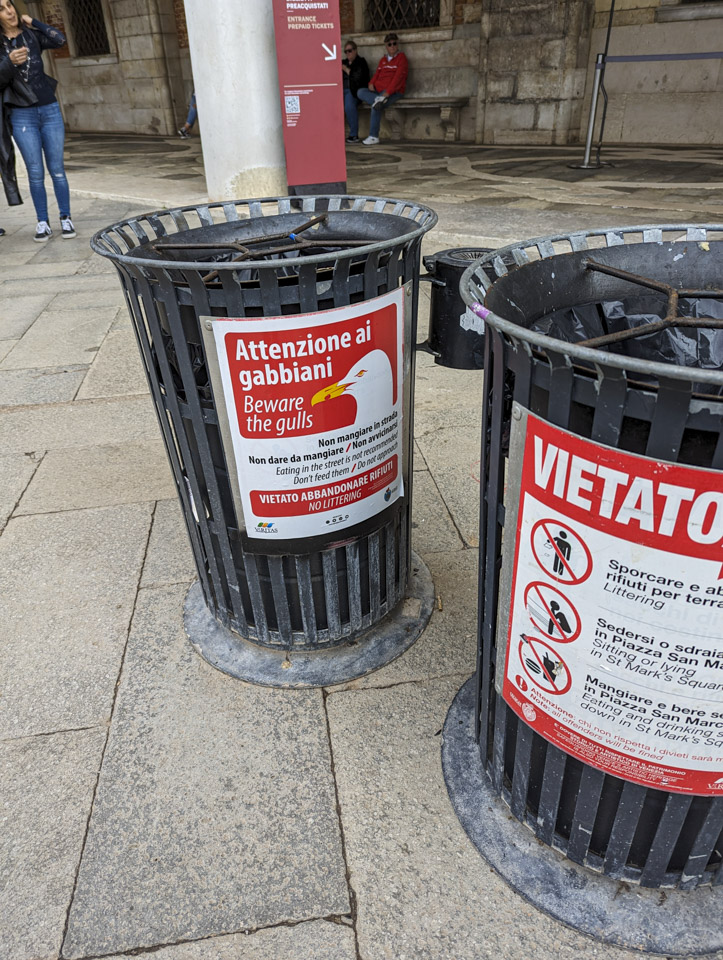 Two trash cans, one of which states in multiple languages not to feed the gulls.