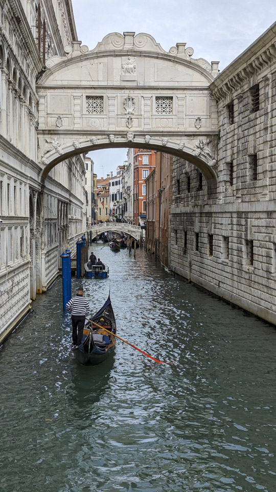 Looking down a canal with a stone passage doing between buildings.