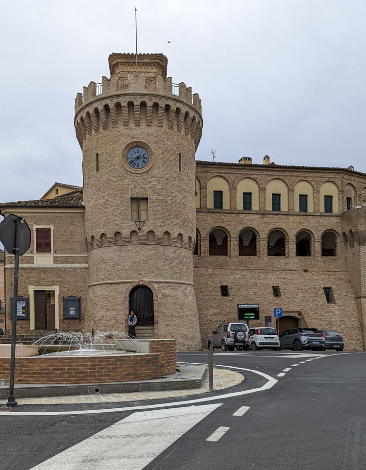 A fountain with the large city walls behind it, and Anne looking small while standing in a doorway.
