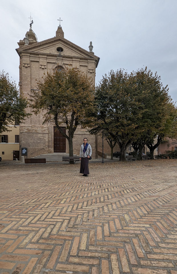 Anne on a piazza with some trees and a church